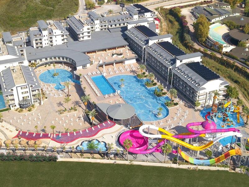 Grande resort con più edifici, piscine e scivoli d'acqua colorati in posizione soleggiata.