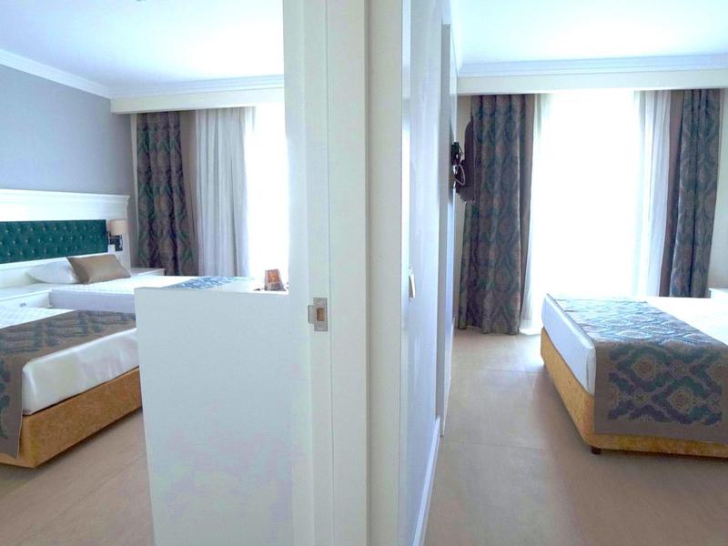 Due camere d'hotel moderne con grandi letti e tende, separate da un muro.