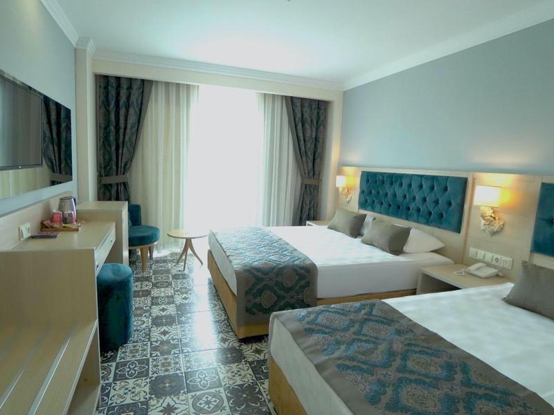 Camera d'hotel moderna con due letti singoli, pavimento moquette e grande finestra con tende.