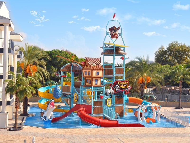 Area giochi acquatica colorata con scivoli e strutture per arrampicata accanto alla piscina dell'hotel sotto un cielo sereno.