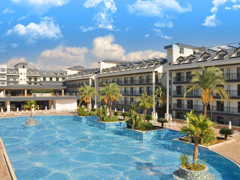 Grande piscina all'aperto davanti a un edificio alberghiero a più piani sotto un cielo blu con nuvole.