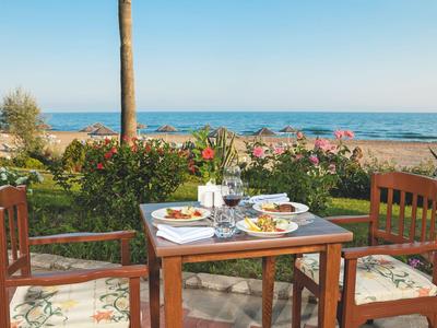 Une table dressée avec le petit-déjeuner sur une terrasse donnant sur la mer avec des fleurs en fleurs.