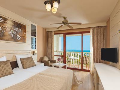 Licht ingericht hotelkamer met groot bed en balkon met uitzicht op zee.