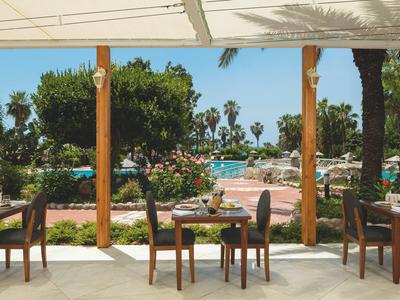 Gemütliche Terrasse mit Tischen und Stühlen, Blick auf Pool und Garten mit Palmen.