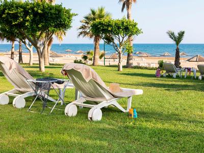 Deux chaises longues et une table sur une pelouse verte avec vue sur la mer et des palmiers.