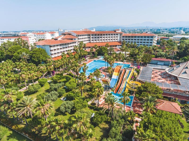 Groot hotelresort met meerdere gebouwen, palmbomen en kleurrijke glijbanen in waterpark.