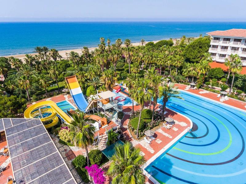 Uitzicht op een waterpark met glijbanen en zwembad, omringd door palmbomen en een hotelgebouw.