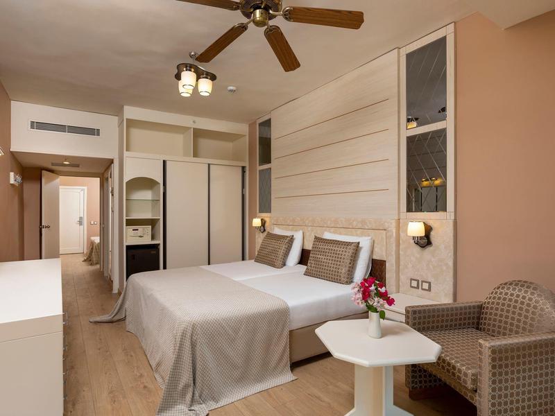 Moderne hotelkamer met tweepersoonsbed, plafondventilator en gezellige zithoek.