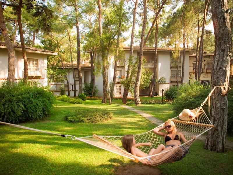 Two people relaxing in hammocks in a green garden area in front of a hotel building.