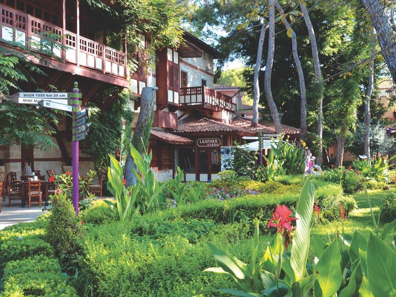 Hotel building with balconies, surrounded by green plants and a well-maintained garden in daylight.