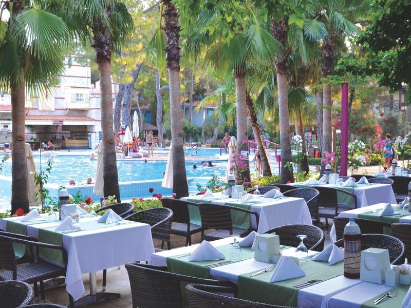 Restaurant terrace with set tables overlooking a pool and palm trees.
