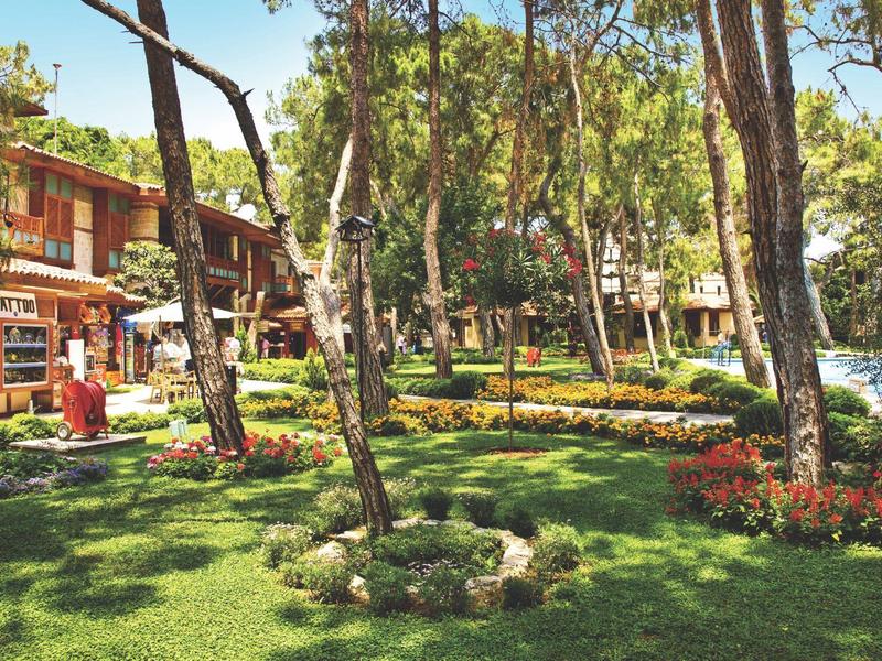 Green hotel garden with trees, flower beds, and buildings in the background on a sunny day