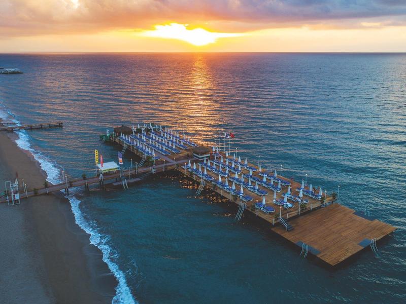 Sunset over a pier with sun loungers on calm sea and sandy beach.