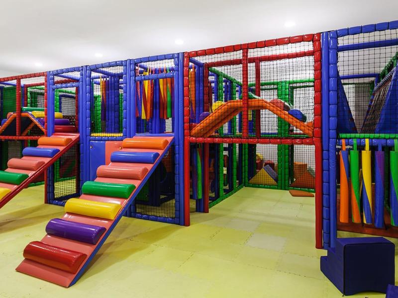 Colorful indoor playground with climbing structures and slides in a hotel or leisure center.