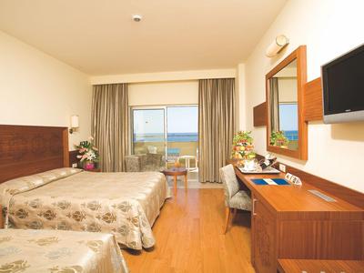 Pokój hotelowy z dwoma łóżkami, biurkiem, telewizorem i widokiem na morze z balkonu.