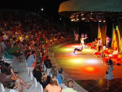 Przedstawienie teatralne przed dużą publicznością w wieczornym amfiteatrze z kolorowymi światłami.