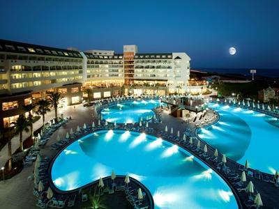 Oświetlony hotelowy basen o zaokrąglonym kształcie nocą pod czystym niebem i pełnią księżyca.