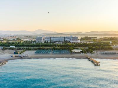 Kurort nadmorski z budynkami hotelowymi, basenem i molo nad spokojnym morzem o zachodzie słońca.