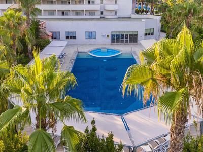 Widok na duży niebieski basen z palmami i białym budynkiem hotelu w tle.