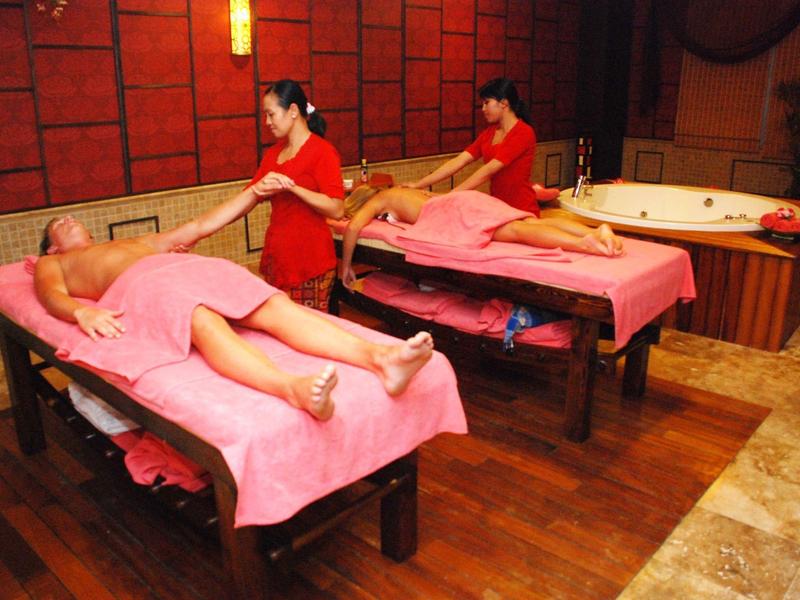 Dwie kobiety otrzymują masaże na różowych stołach do masażu w spa z jacuzzi w pobliżu.