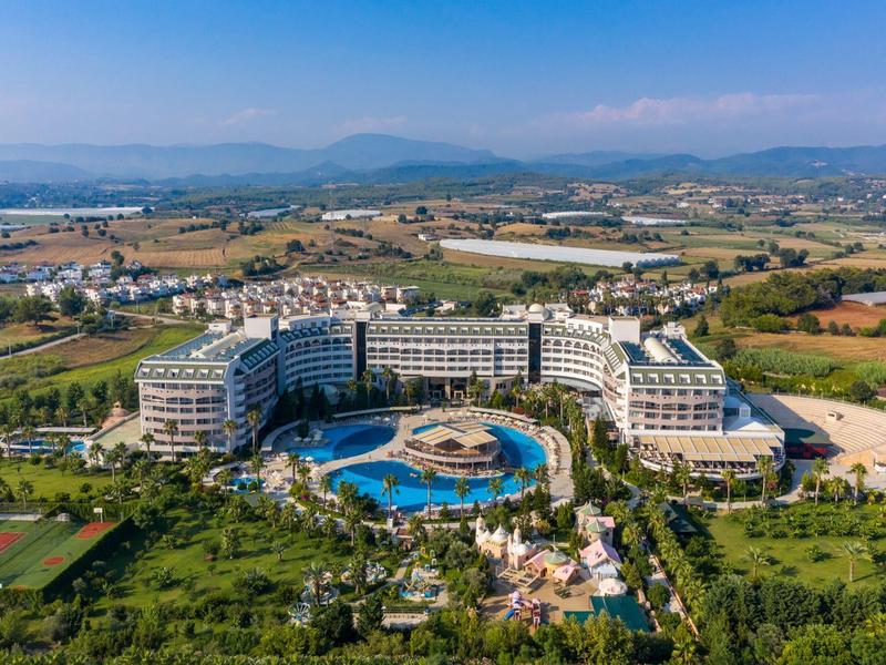 Duży ośrodek hotelowy z basenem na obszarze wiejskim, z górami w tle.