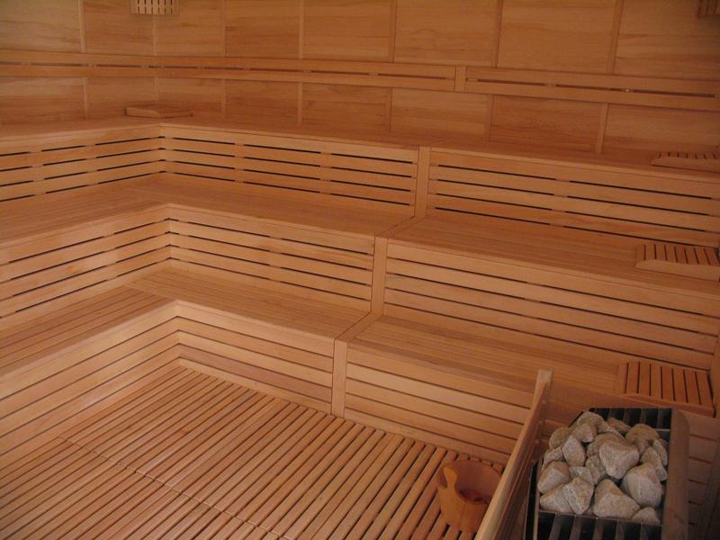 Strefa sauny z drewnianymi ławkami i piecem na kamienie