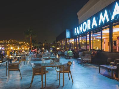 Terrasse d'un restaurant de nuit avec tables, chaises et vue panoramique sur les lumières de la ville.