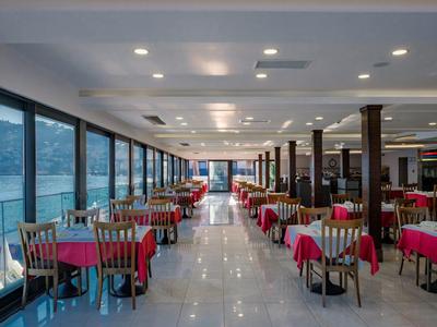 Grand restaurant avec nappes rouges et fenêtres panoramiques offrant une vue sur la mer.