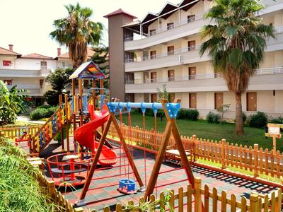 Aire de jeux pour enfants avec toboggans et balançoires à côté d'un hôtel à plusieurs étages.