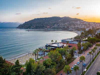 Plage et ville côtière au coucher du soleil avec arbres verts et routes au bord de l'eau.