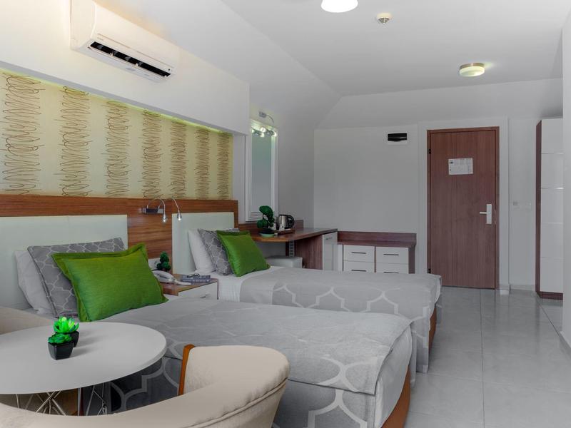 Chambre d'hôtel moderne avec deux lits, accents verts et intérieur lumineux.