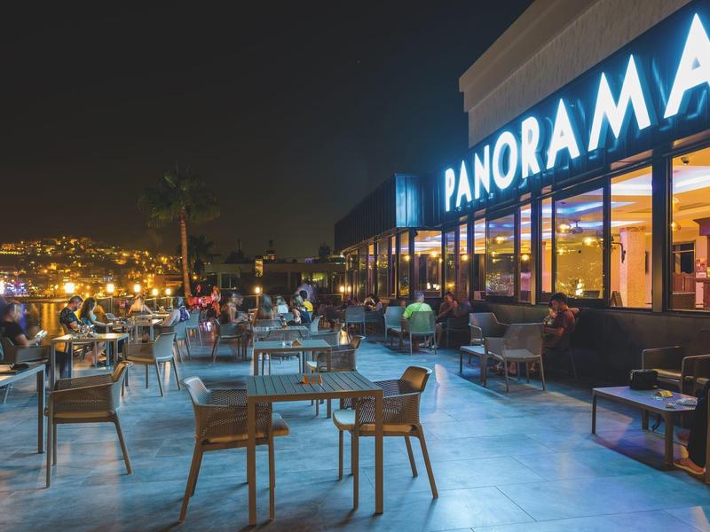 Terrasse d'un restaurant de nuit avec tables, chaises et vue panoramique sur les lumières de la ville.
