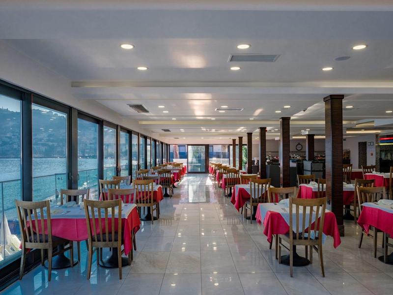 Grand restaurant avec nappes rouges et fenêtres panoramiques offrant une vue sur la mer.