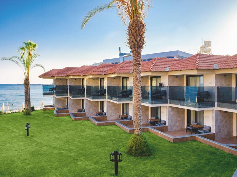 Bâtiment d'hôtel en bord de mer avec pelouse verte et palmiers.