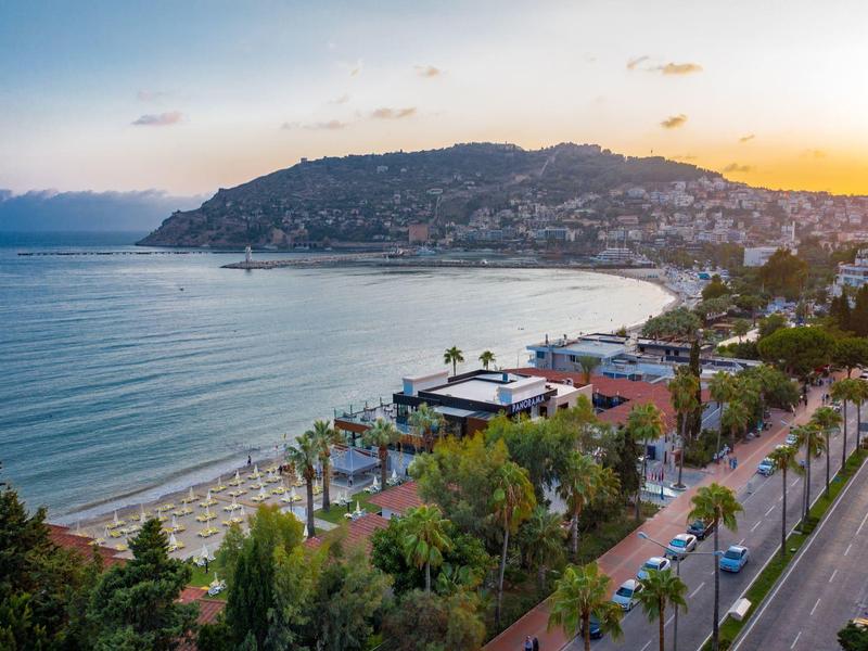 Plage et ville côtière au coucher du soleil avec arbres verts et routes au bord de l'eau.