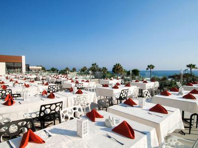 Velká terasa s bílými prostřenými stoly s výhledem na moře za jasné oblohy.