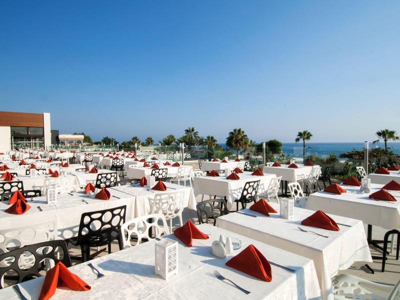 Velká terasa s bílými prostřenými stoly s výhledem na moře za jasné oblohy.