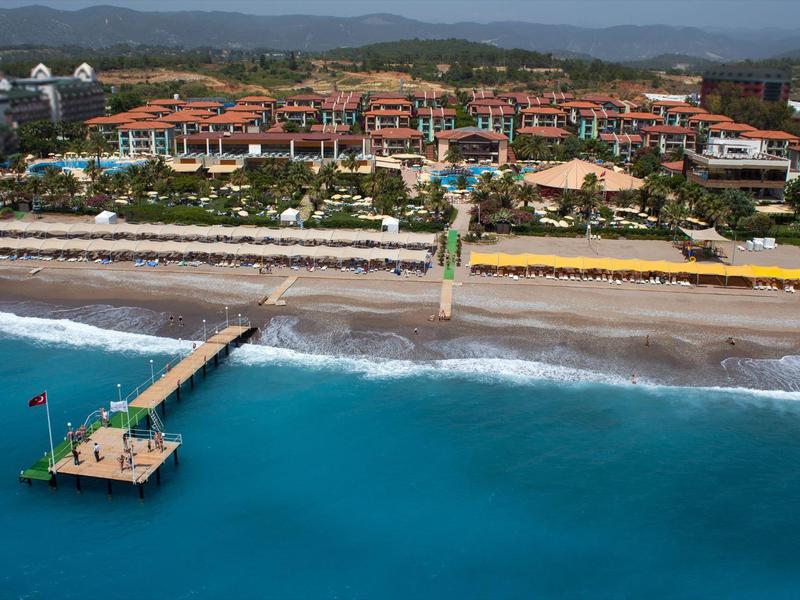 Resort s pláží, bazénem a molem u tyrkysového moře s horským pozadím