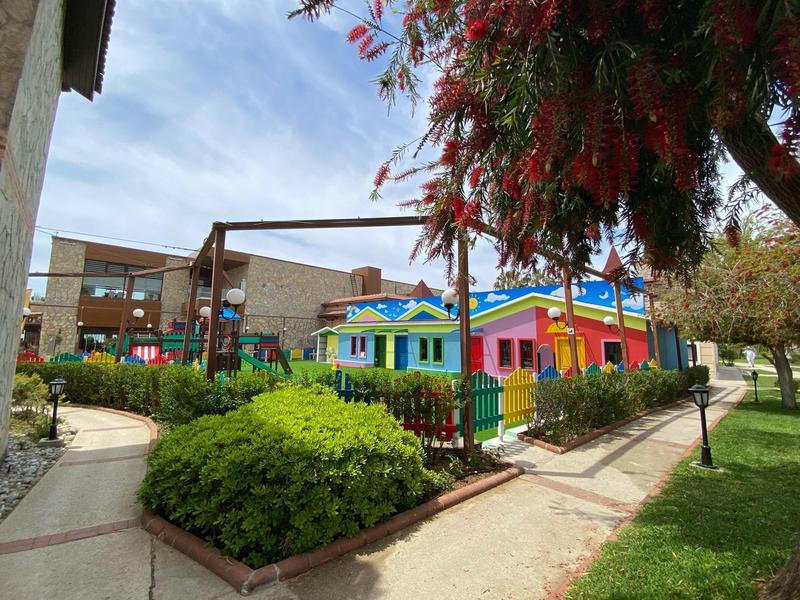 Barevné budovy a dětské hřiště v zahradní části hotelu za slunečného dne.