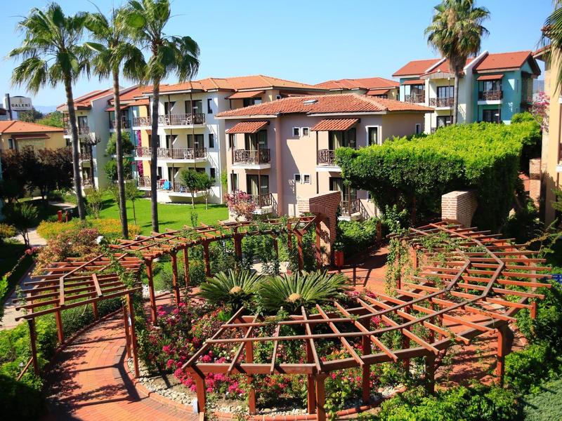 Světelný hotelový komplex s palmami, zalesněnými pergolami a dobře udržovanými cestami.