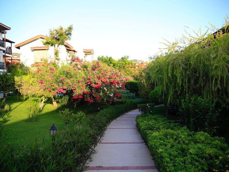 Cesta přes upravenou zahradu s kvetoucími keři vedle hotelových budov.