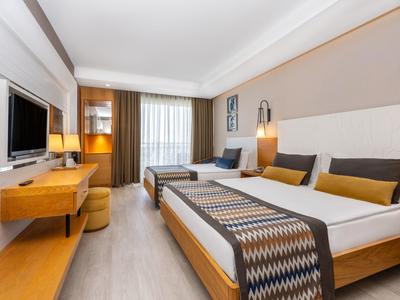 Modern hotel room with double bed, single sofa bed, desk, and large window with curtains.