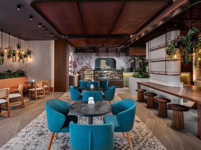 Modern hotel lounge area with blue chairs, wooden tables, and green plants.