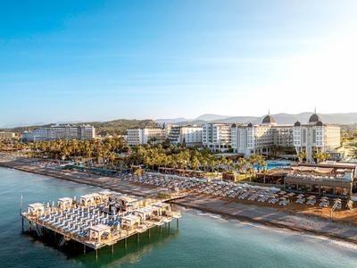 Luxury hotel on the beach with wooden pier and umbrellas over calm blue water.