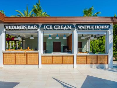Open kiosk offering vitamin bar, ice cream, and waffles in a sunny outdoor setting.