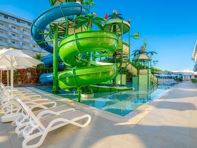 Green water slide tower beside pool with sun loungers and hotel buildings in the background.