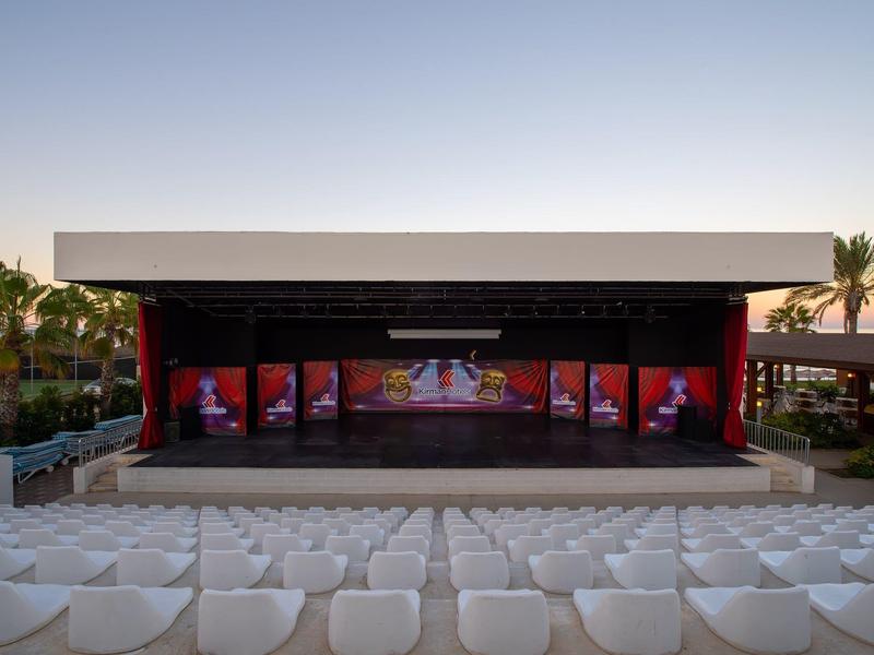 Empty open-air stage with white seating rows in a hotel garden at sunset