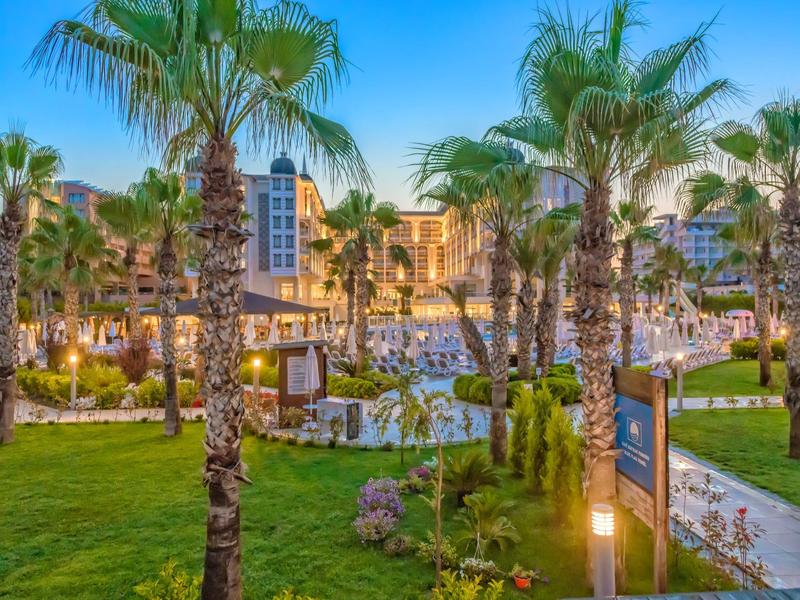 Evening view of a resort with palm trees, pool, and garden areas.