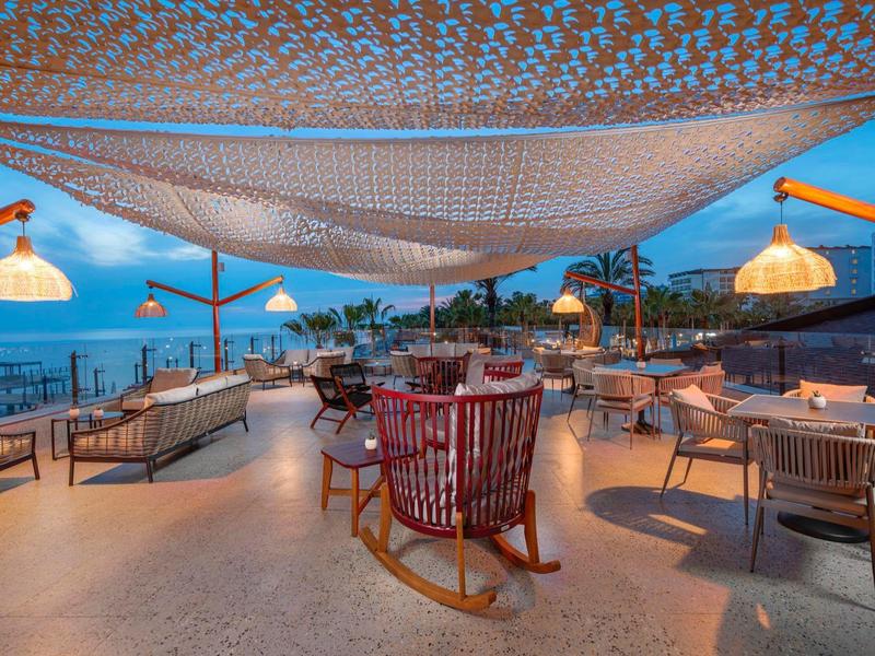 Modern beach terrace with cozy seating areas and decorative lighting at dusk.
