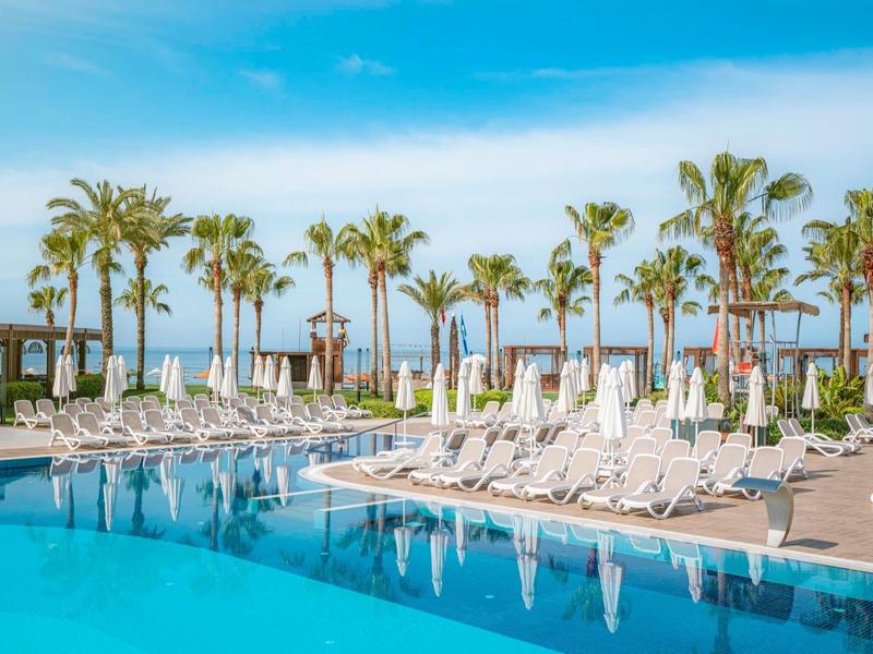 Large hotel pool with sun loungers and palm trees under blue sky.